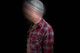 Man wearing a flannel shirt, green shirt, and beanie in a dark room.